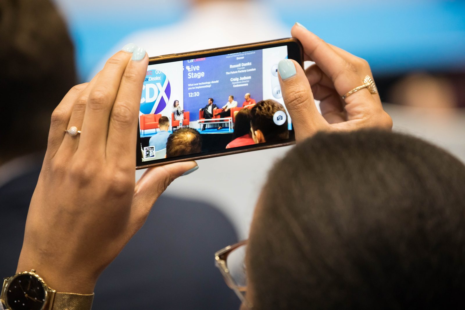 An audience member photographing a panel discussion on their phone